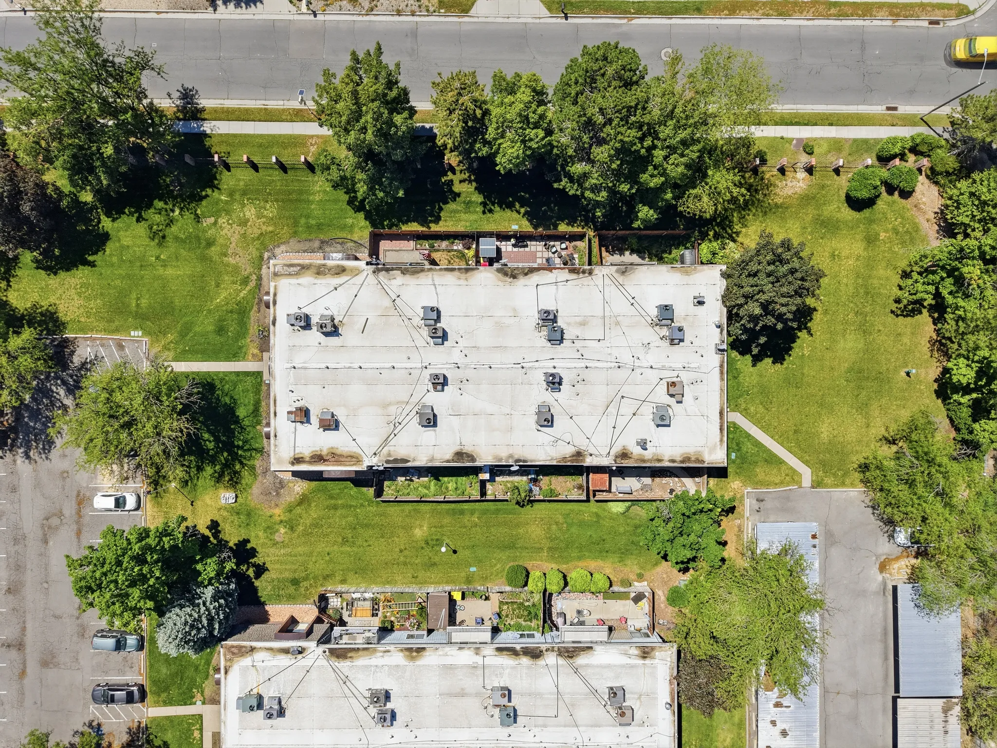 Expansive rooftop with multiple HVAC units and visible conduit, surrounded by a large grassy area with mature trees and paved parking