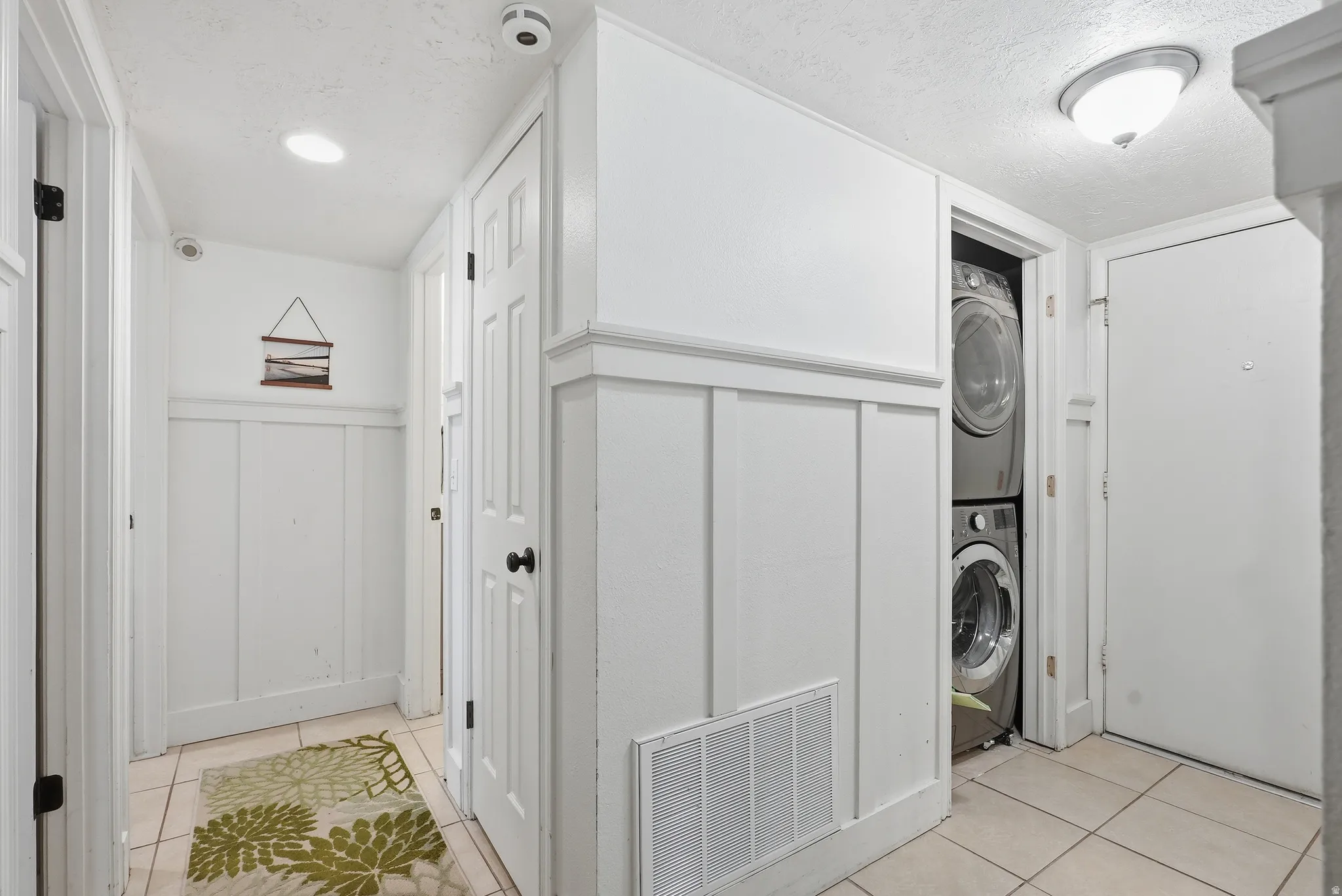 Hallway featuring board and batten paneling, tile flooring, recessed lighting, and a built-in stacked washer and dryer unit