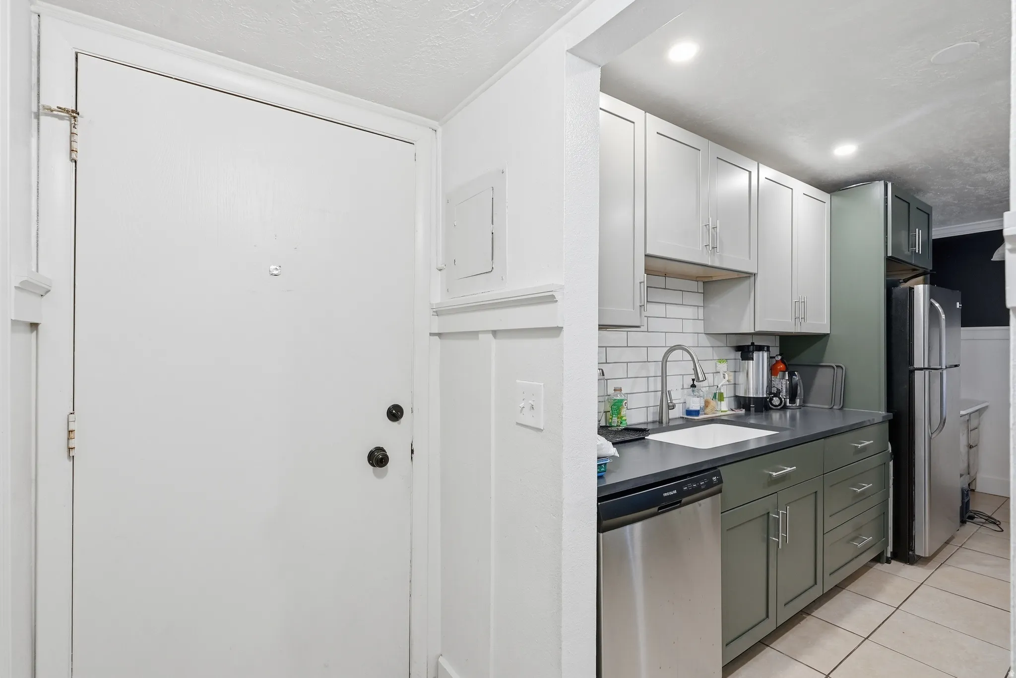 Kitchen featuring two-tone cabinetry with light upper and dark lower units, stainless steel dishwasher, and a subway tile backsplash
