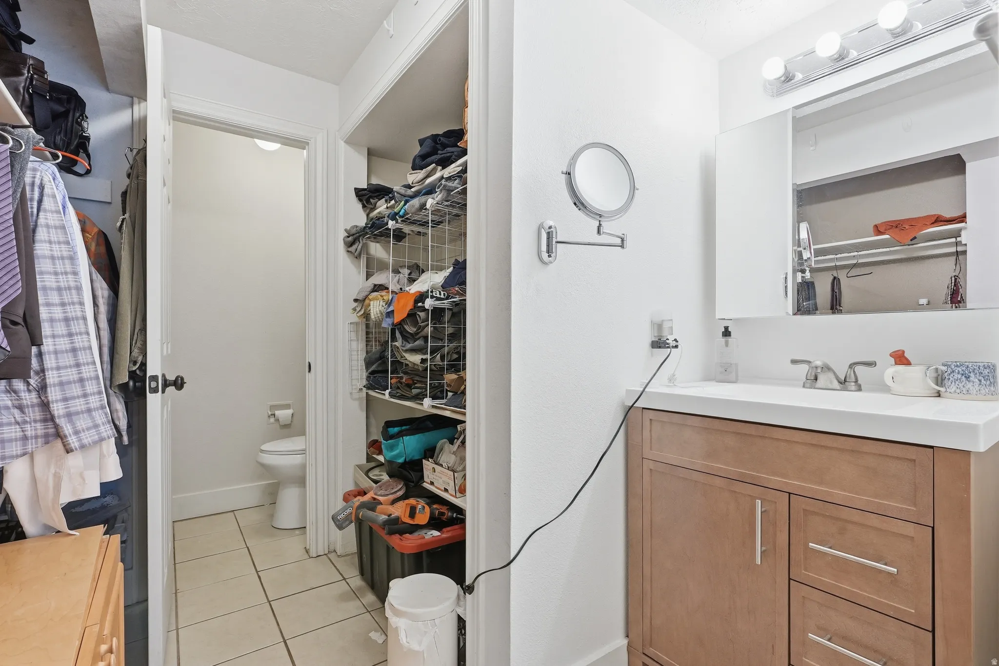 Bathroom vanity featuring a single sink, light wood-finish cabinetry with silver-tone hardware, and a white countertop