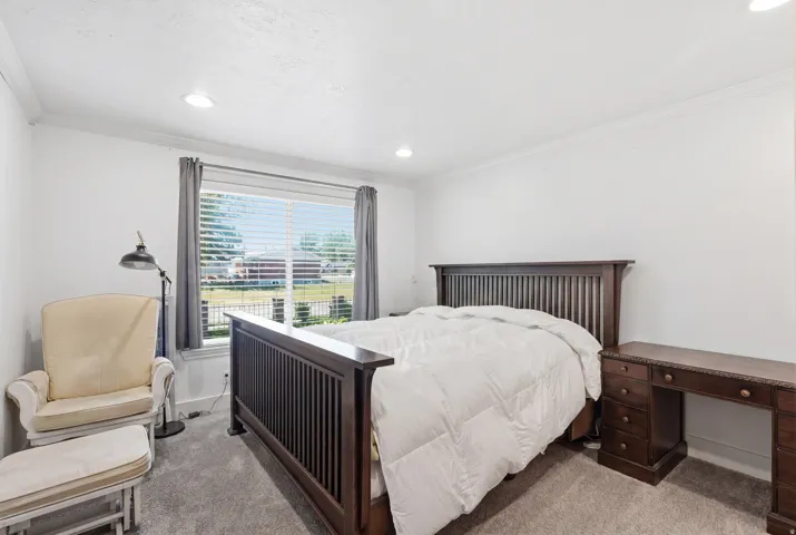 Spacious bedroom featuring clean white walls, recessed lighting, crown molding, and plush gray carpeting