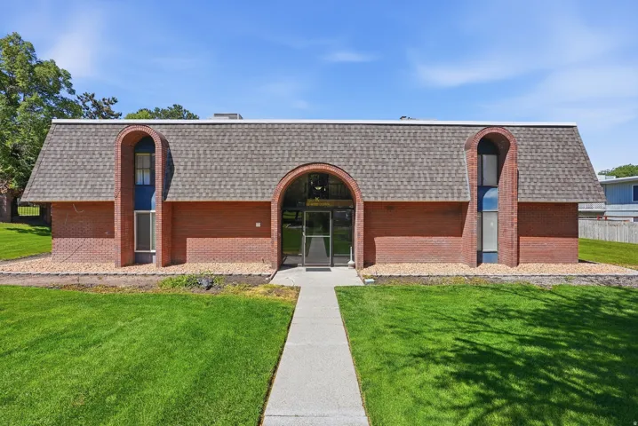 Brick facade building with an arched entryway and matching dormers, set amidst a vibrant green lawn and a concrete walkway