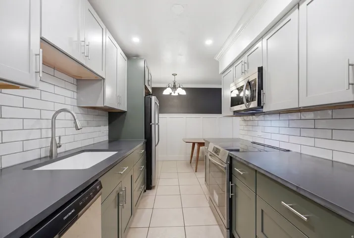 Galley kitchen featuring dual-tone cabinetry, subway tile backsplash, and dark countertops