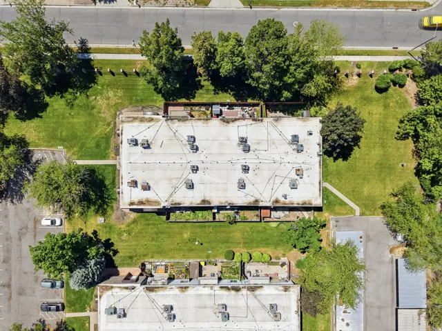 Expansive rooftop with multiple HVAC units and visible conduit, surrounded by a large grassy area with mature trees and paved parking