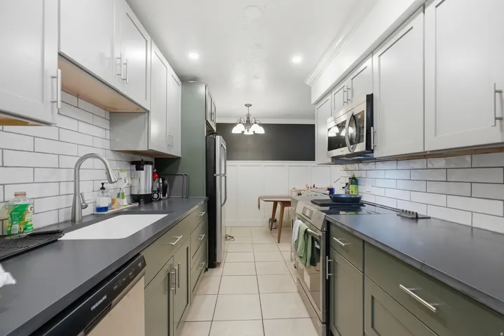 Galley kitchen featuring two-tone cabinetry, white subway tile backsplash, and dark countertops