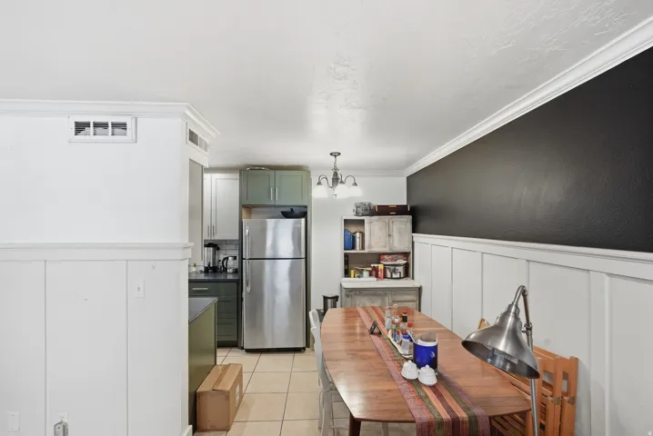 Open-concept kitchen and dining area featuring board and batten paneling, crown molding, stainless steel refrigerator, and tiled flooring