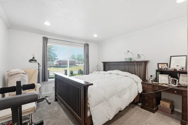 Bright room featuring a large window with blinds, recessed lighting, crown molding, and carpeted flooring