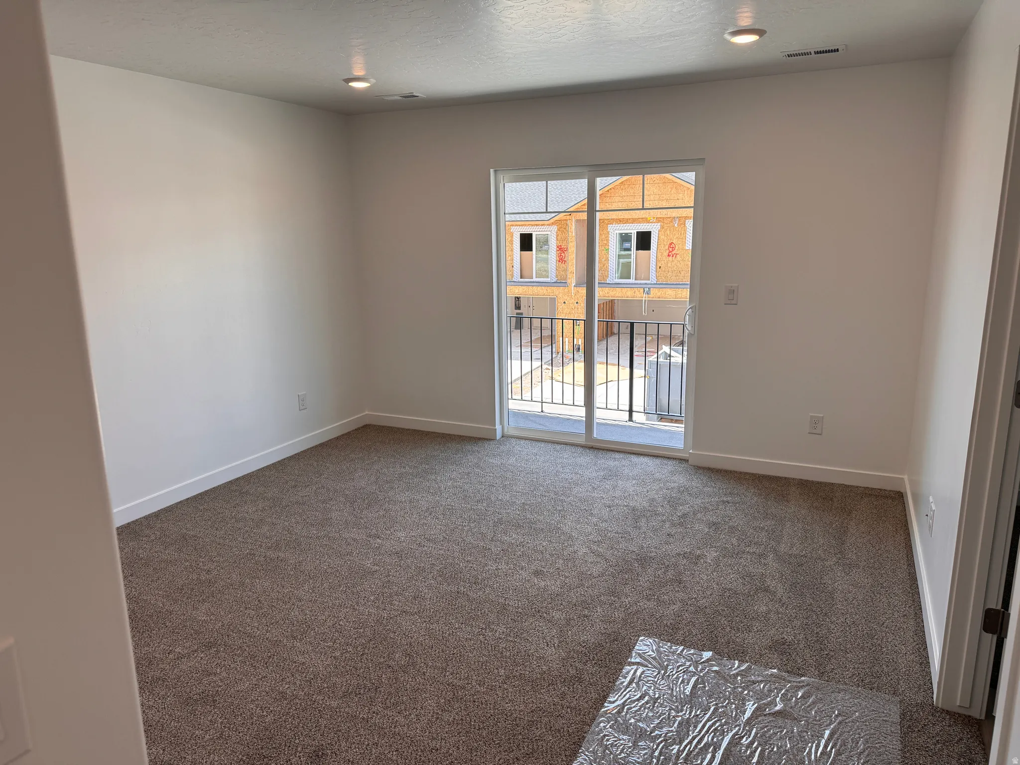 Spacious room featuring neutral carpeting, white baseboards, recessed ceiling lighting, and a sliding glass door providing balcony access