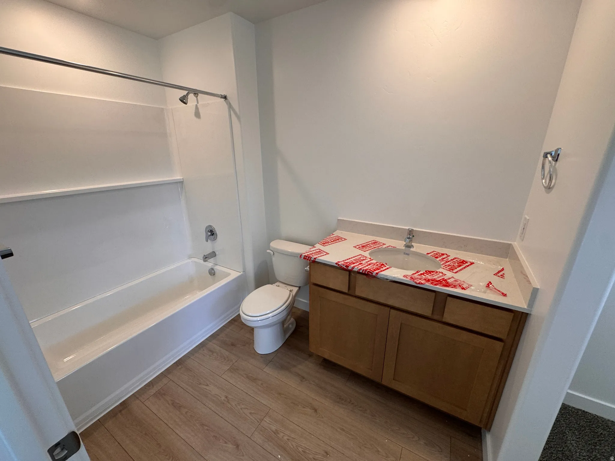 Full bathroom featuring a white tub and shower combination with chrome fixtures, a wood-finish vanity with a single sink and light-toned countertop, and wood-finish flooring