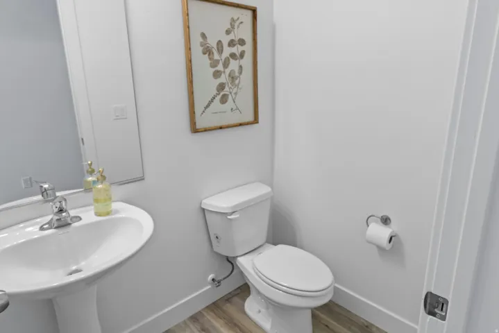 Pedestal sink with chrome faucet and white toilet set against light wood-finish flooring