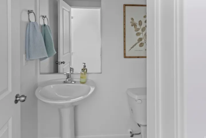 Pedestal sink with chrome faucet, mirror, and toilet, all set against white walls
