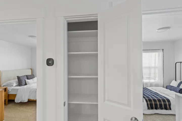 Central hallway featuring an open linen closet with integrated shelving, a wall-mounted thermostat, and two separate rooms with white paneled doors