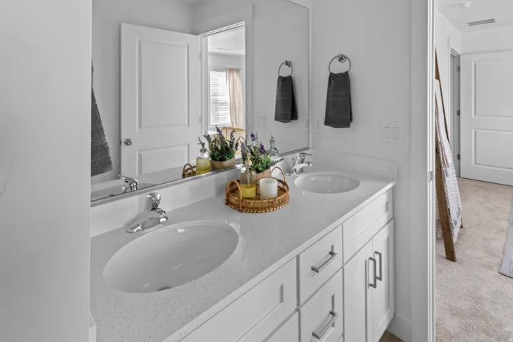 Dual undermount sinks set into a light-toned countertop, featuring polished chrome faucets and white shaker-style cabinetry with brushed nickel hardware