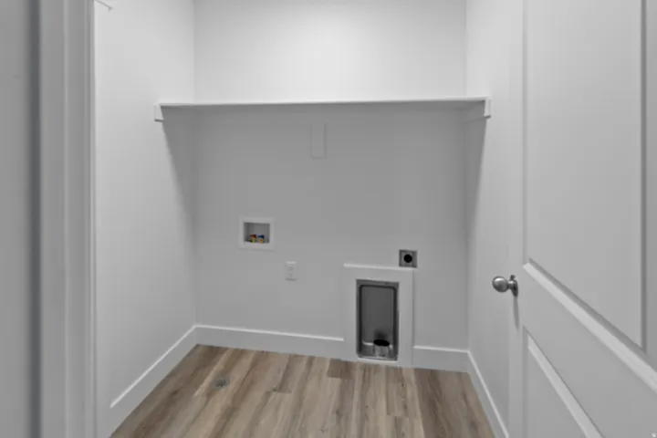 Dedicated laundry area featuring wood-finish flooring, a wall-mounted utility shelf, and white baseboards