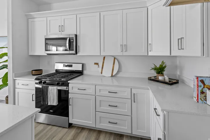 Modern kitchen featuring white shaker cabinetry, light-toned countertops, stainless steel appliances, wood-finish flooring, and contemporary hardware