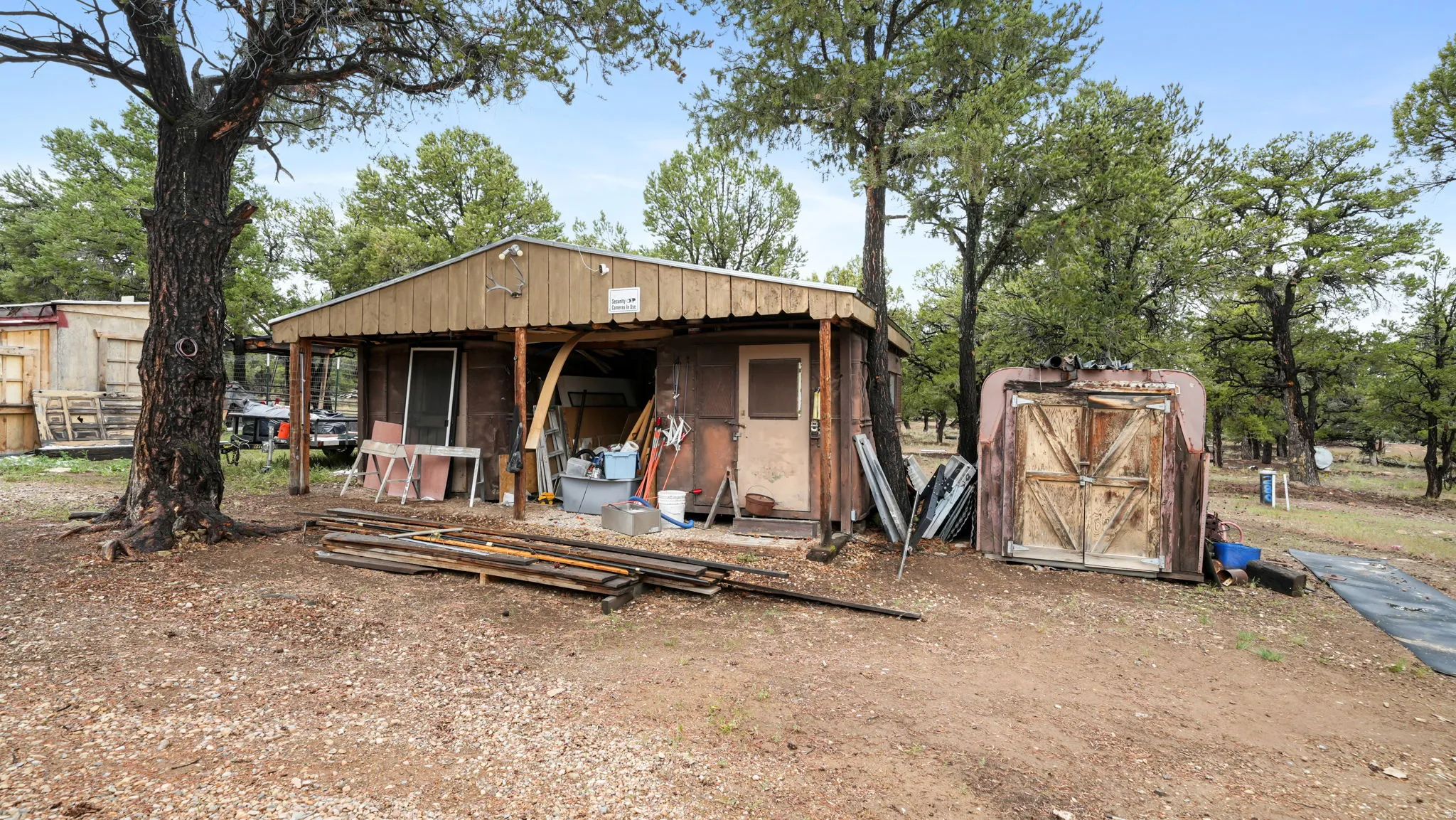 Metal-sided structure featuring a covered porch area and a separate storage shed with double wooden doors