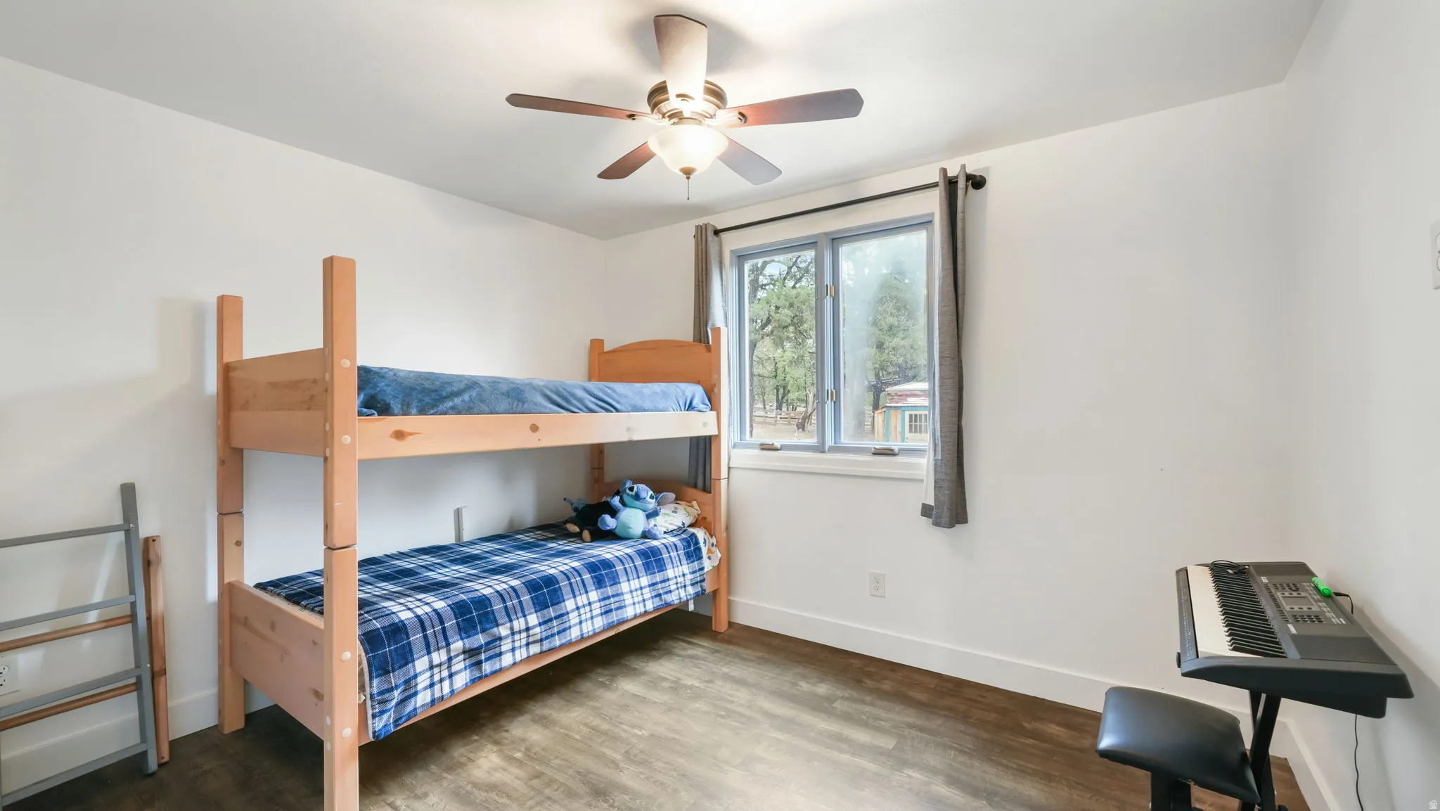 Bright room featuring wood-finish flooring, a ceiling fan with integrated lighting, white walls, and a window with trim
