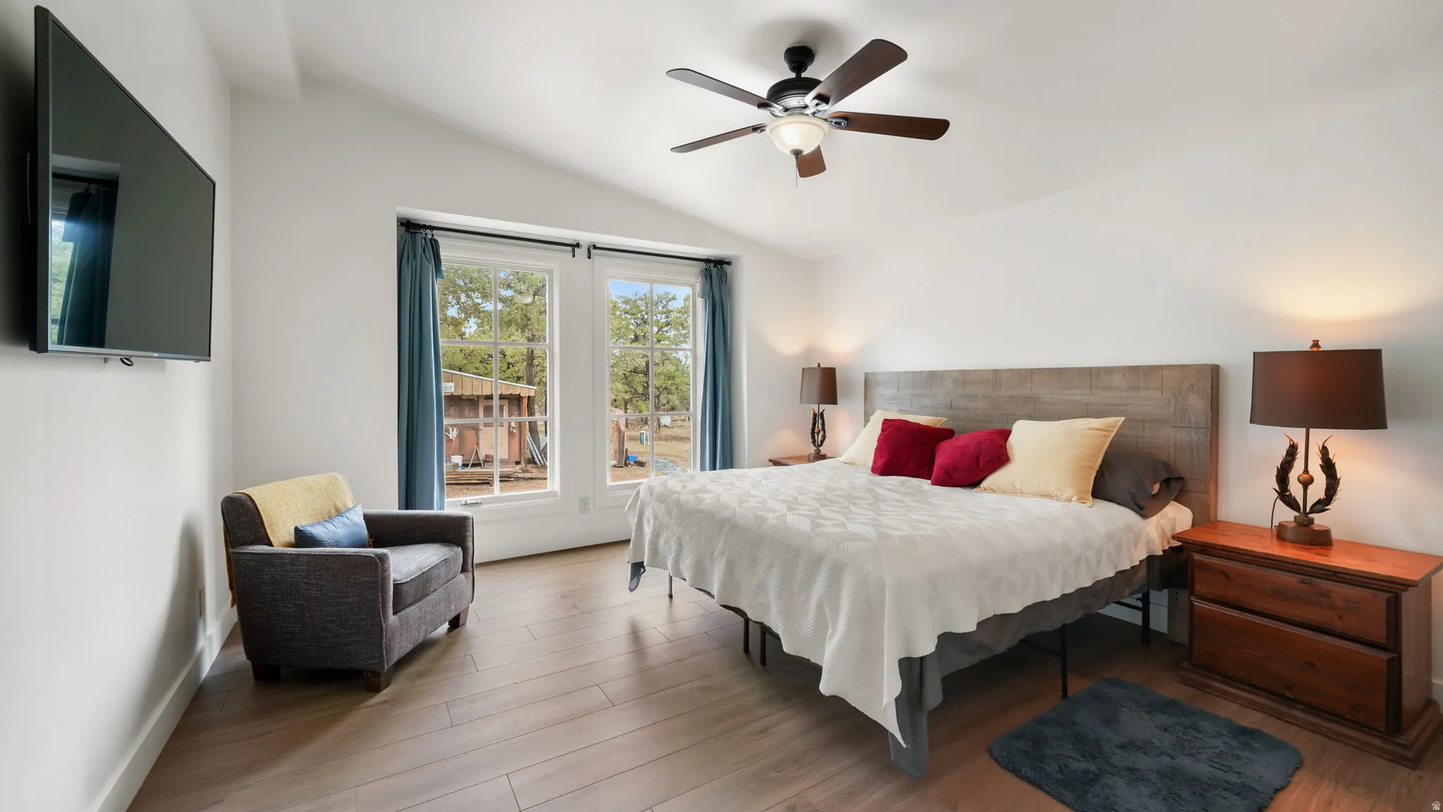 Bedroom featuring vaulted ceilings, wood-finish flooring, dual windows with exterior views, and a ceiling fan with integrated lighting