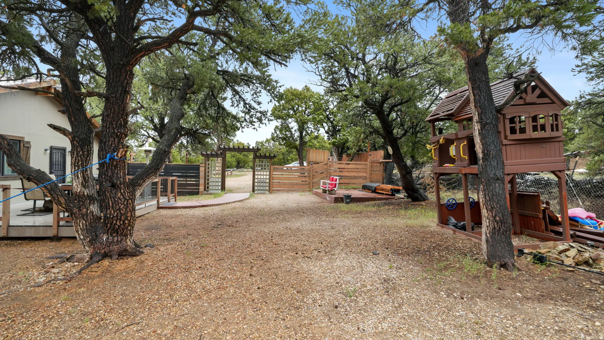 Expansive outdoor space featuring mature trees, a wooden deck, a decorative wooden arbor, and a privacy fence