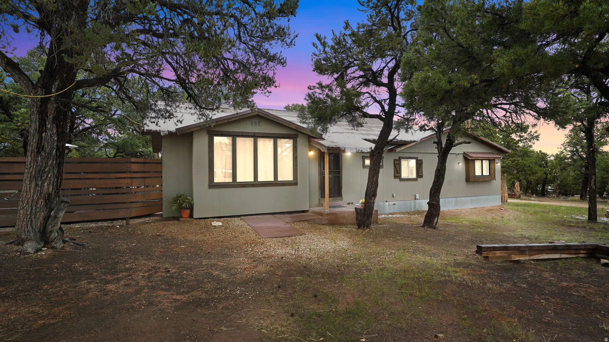 Ranch-style residence featuring a muted green exterior and multiple mature trees