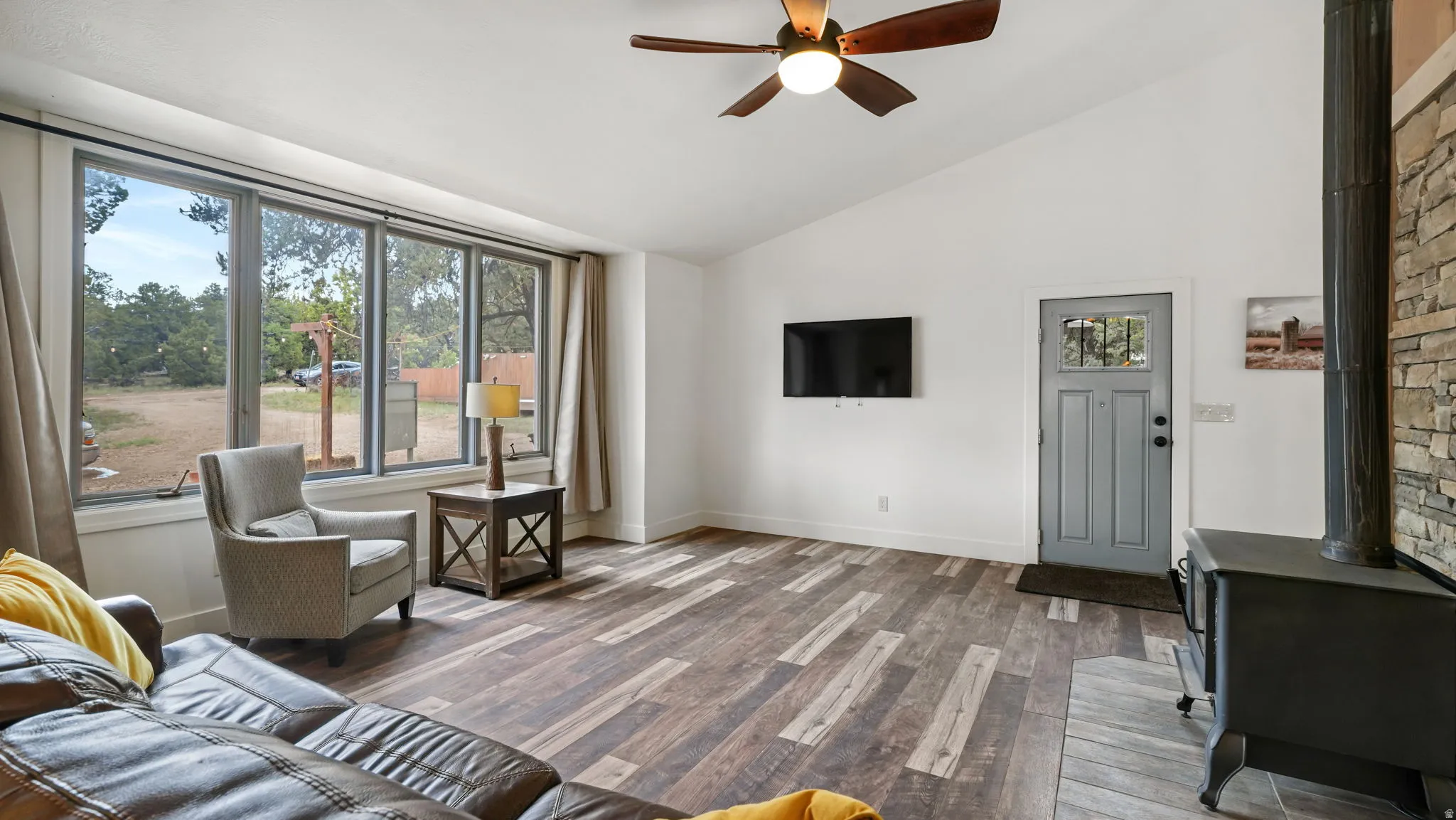 Spacious living area featuring wood-finish flooring, a vaulted ceiling, and a prominent wood-burning stove with stone surround