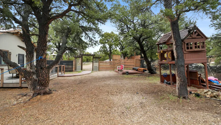 Expansive outdoor space featuring mature trees, a wooden deck, a decorative wooden arbor, and a privacy fence