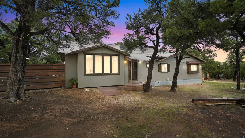 Ranch-style residence featuring a muted green exterior and multiple mature trees