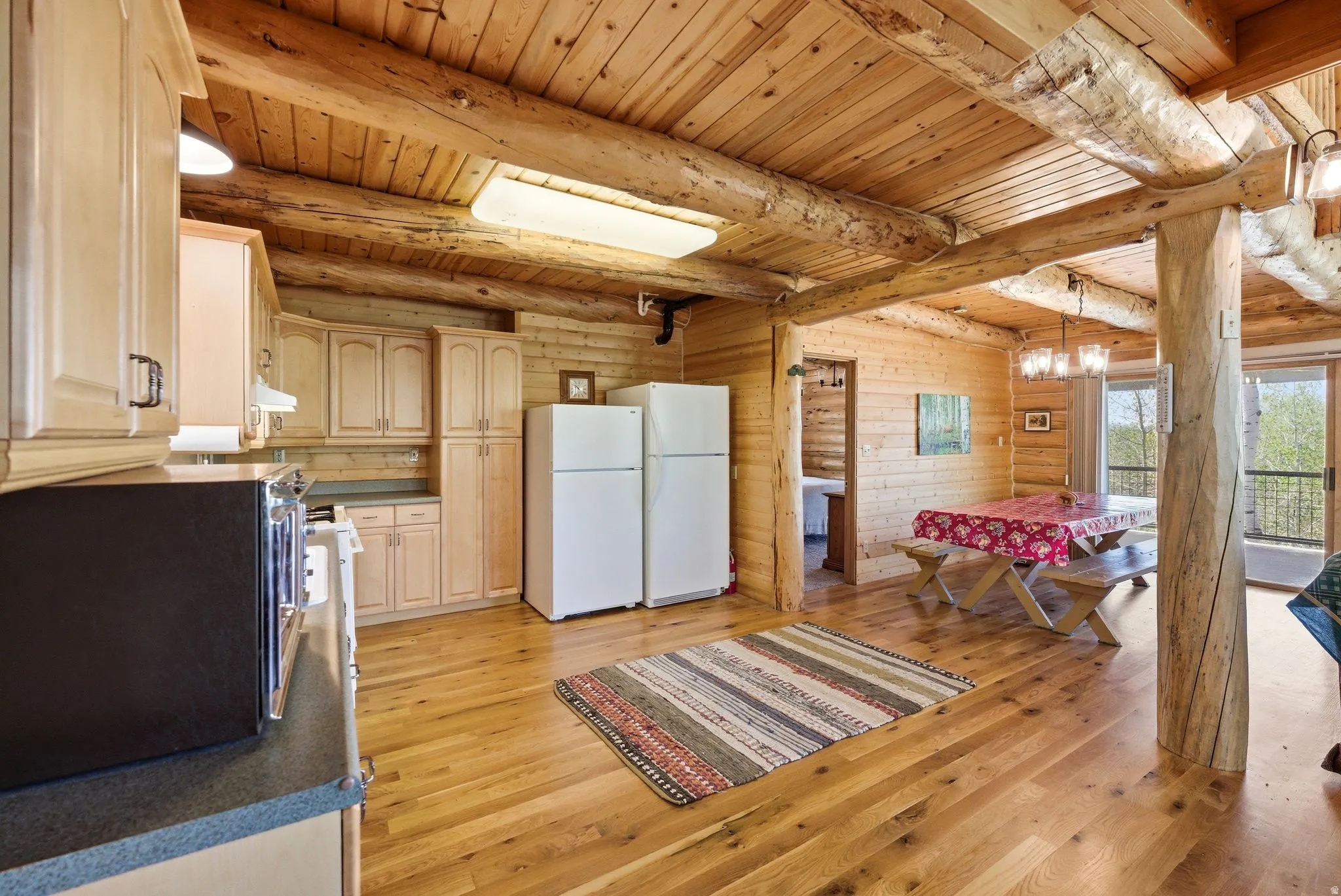 Open-concept living space featuring wood-finish flooring, exposed log beams, and wood paneling throughout