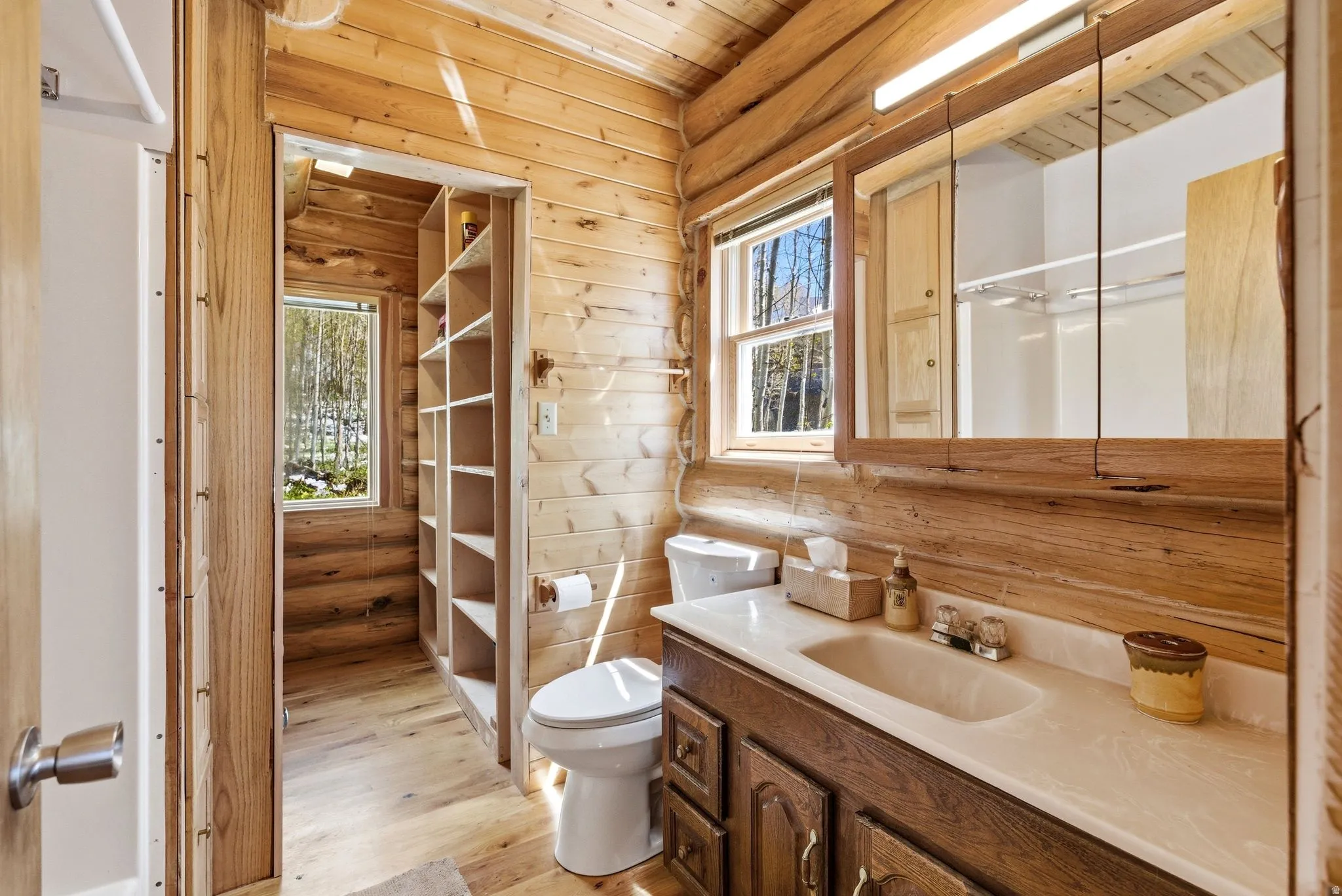 Bathroom featuring wood-finish walls and flooring, a vanity with a built-in sink and storage, a mirrored medicine cabinet, and a window