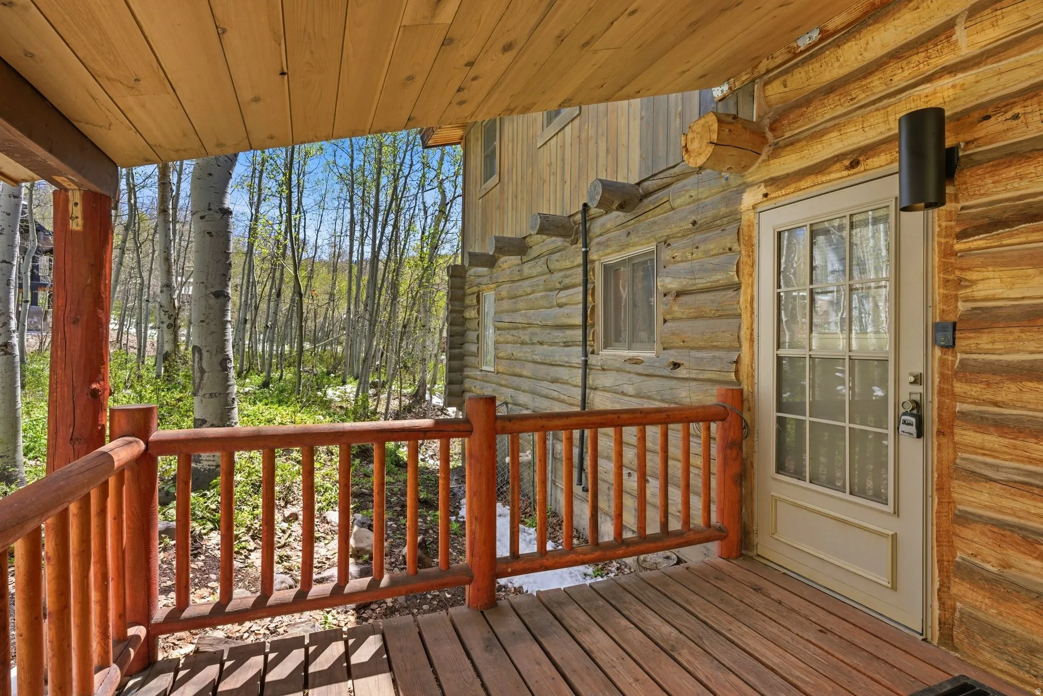Wood deck with log railing, featuring a wood-plank ceiling and a glass-paned exterior door