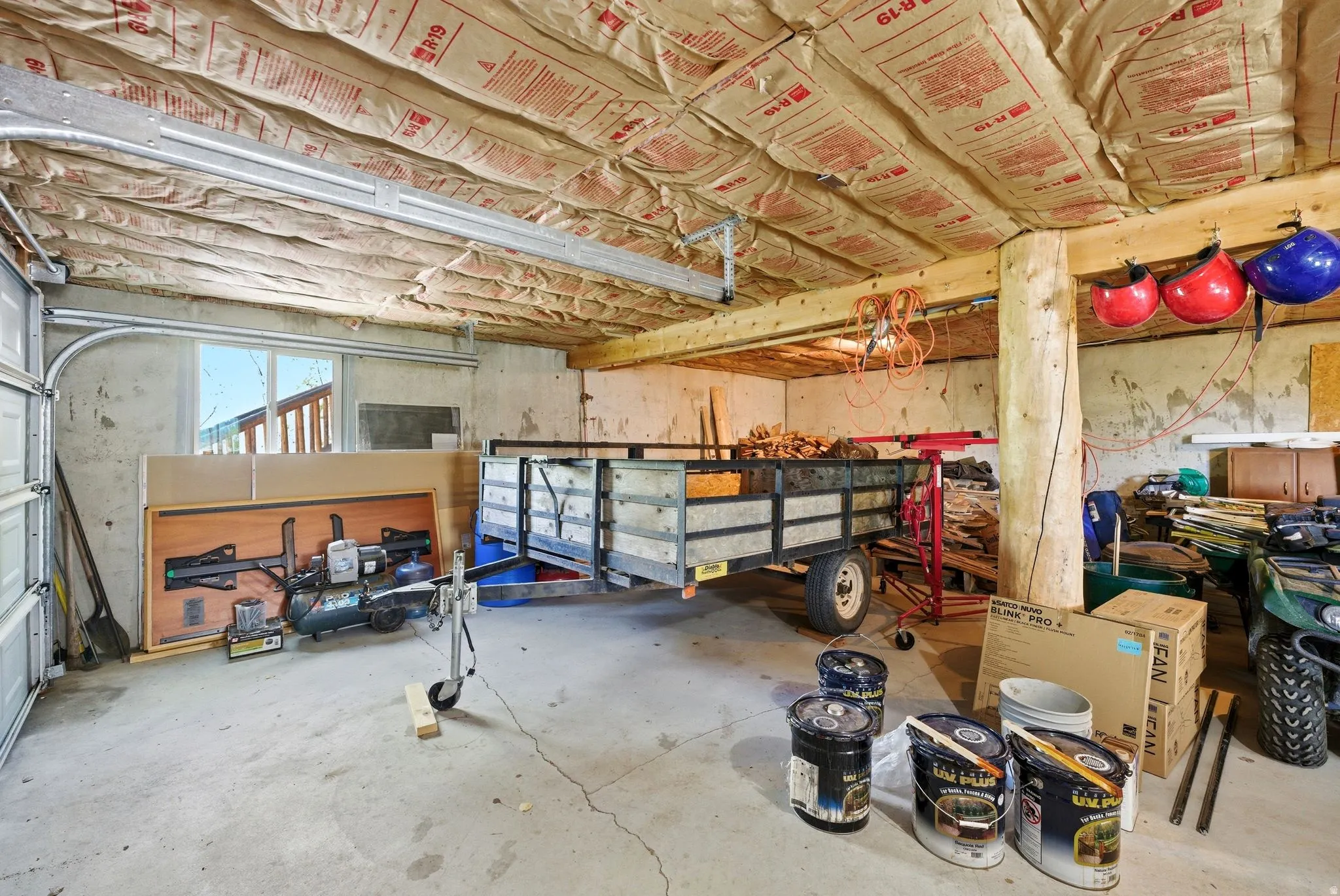 Utility space featuring exposed ceiling insulation, concrete flooring, a garage door, and a support column