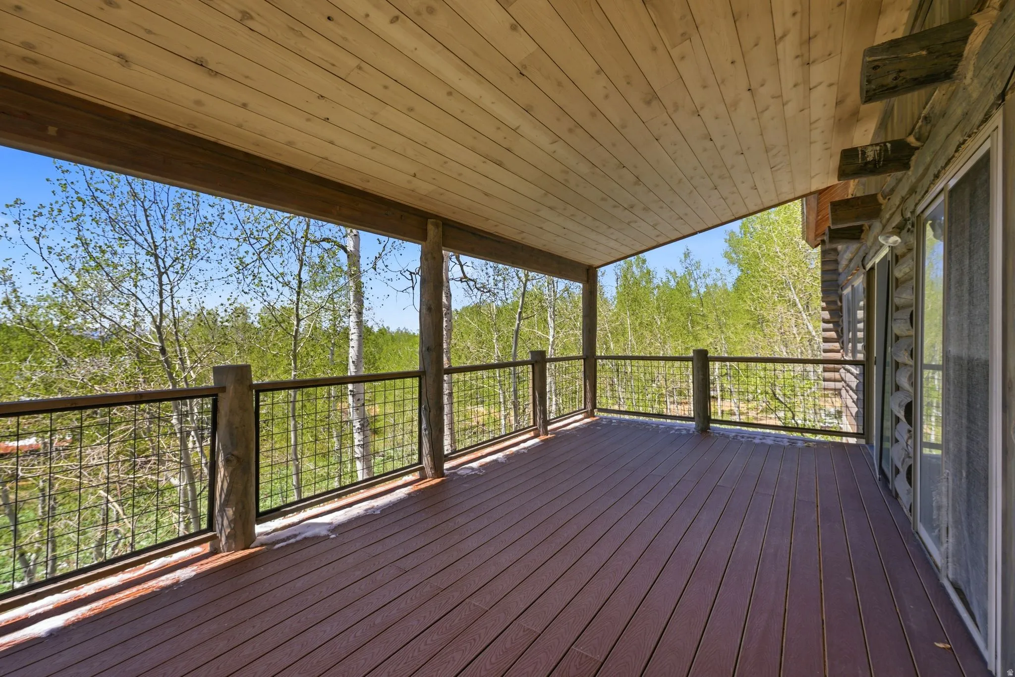 Expansive covered deck featuring wood-finish flooring, natural wood support posts, and black wire railings