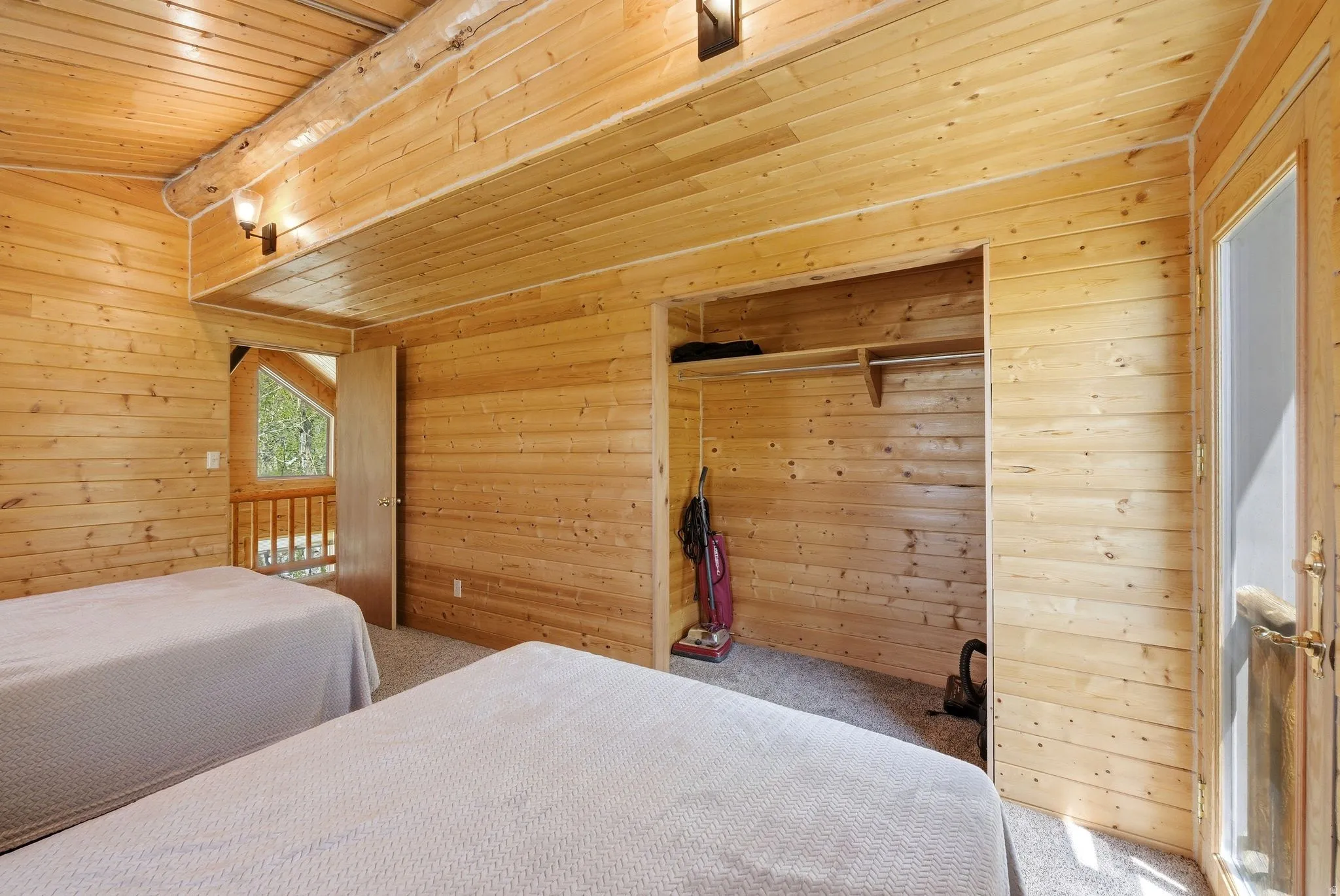 Wood-paneled room featuring a built-in closet with shelving and rod, exposed wood beam, wall-mounted lighting, and a partial glass-paneled door