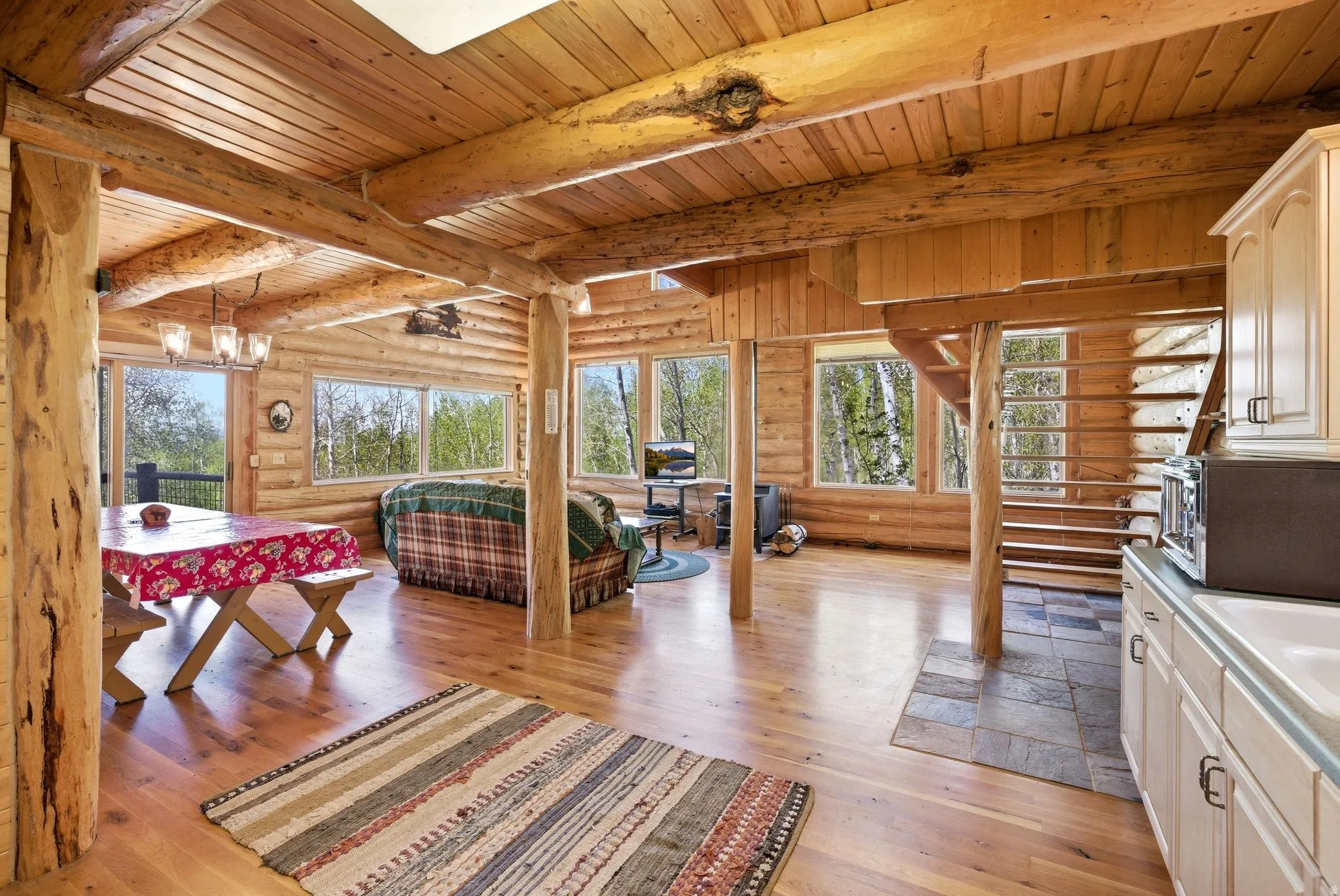 Open-concept living area with extensive natural wood finishes, hardwood flooring, an exposed beam ceiling, built-in cabinetry, and a wood staircase