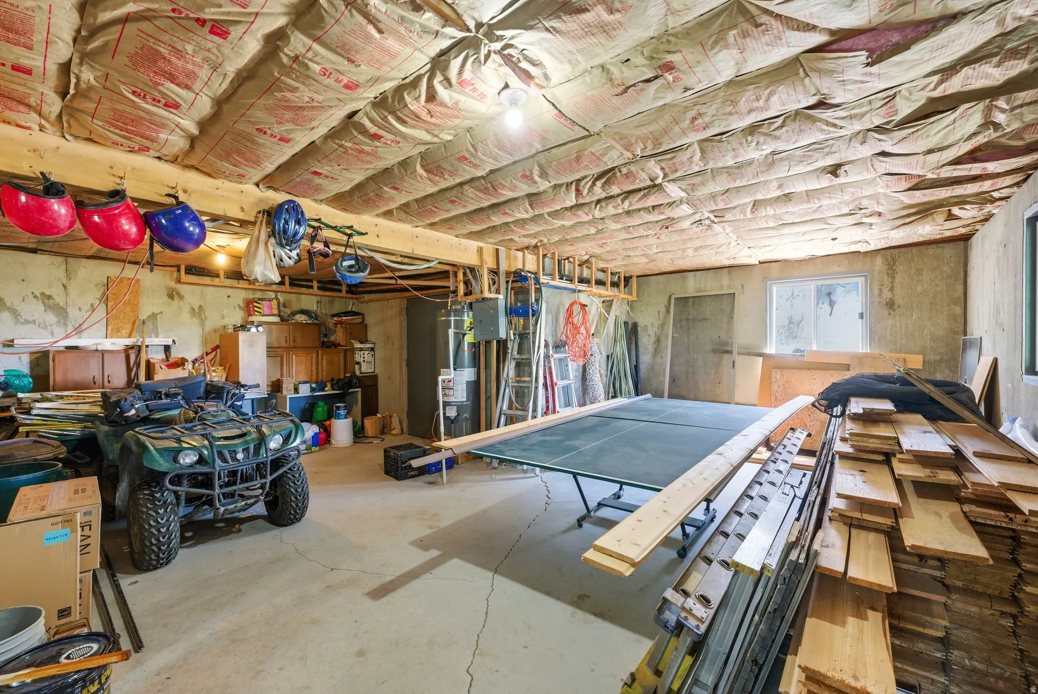 Finished basement space featuring concrete flooring, exposed ceiling insulation, wood beam accents, and a window