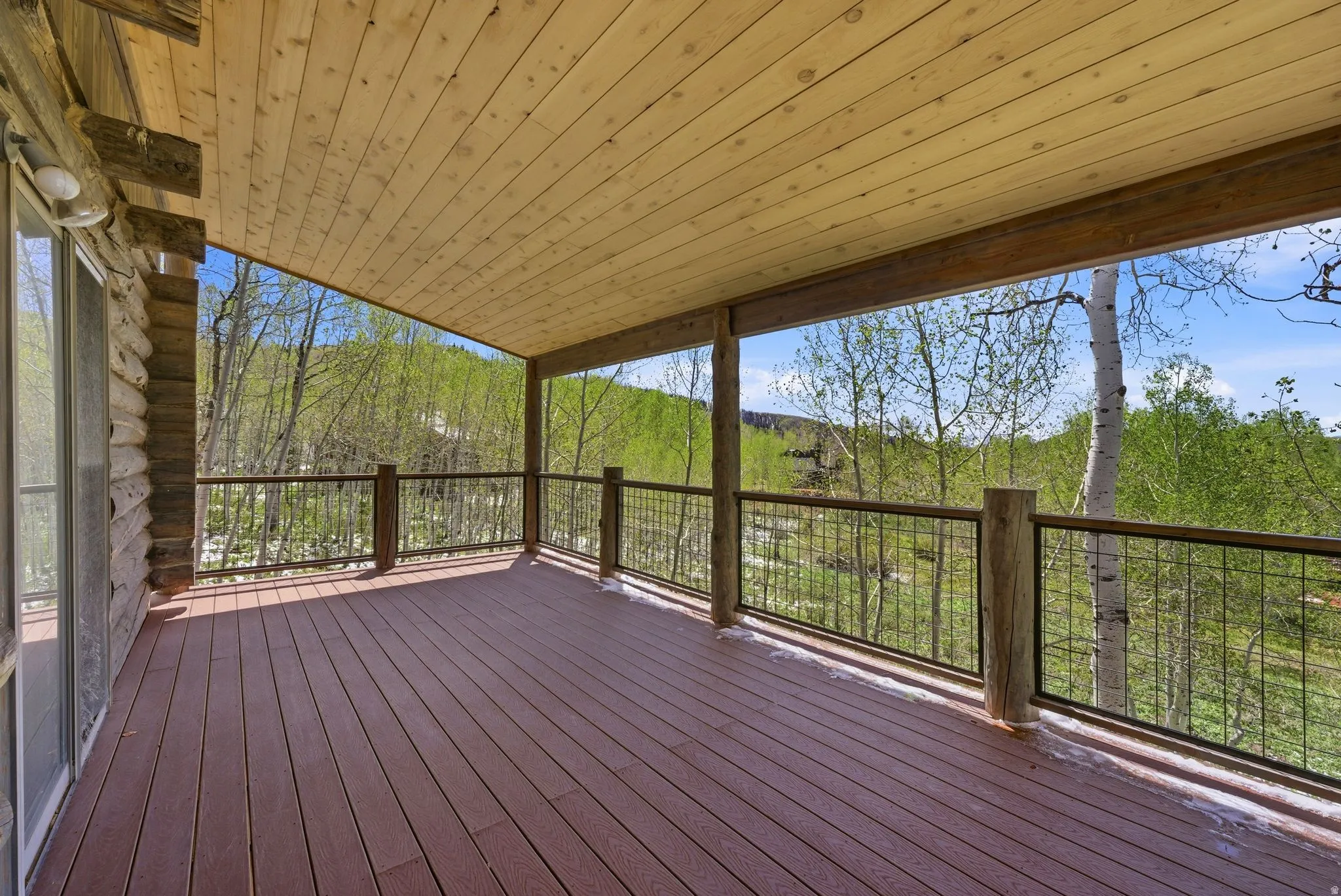 Expansive covered deck featuring wood-finish decking, log accents, a horizontal wire railing, and a tongue-and-groove wood ceiling