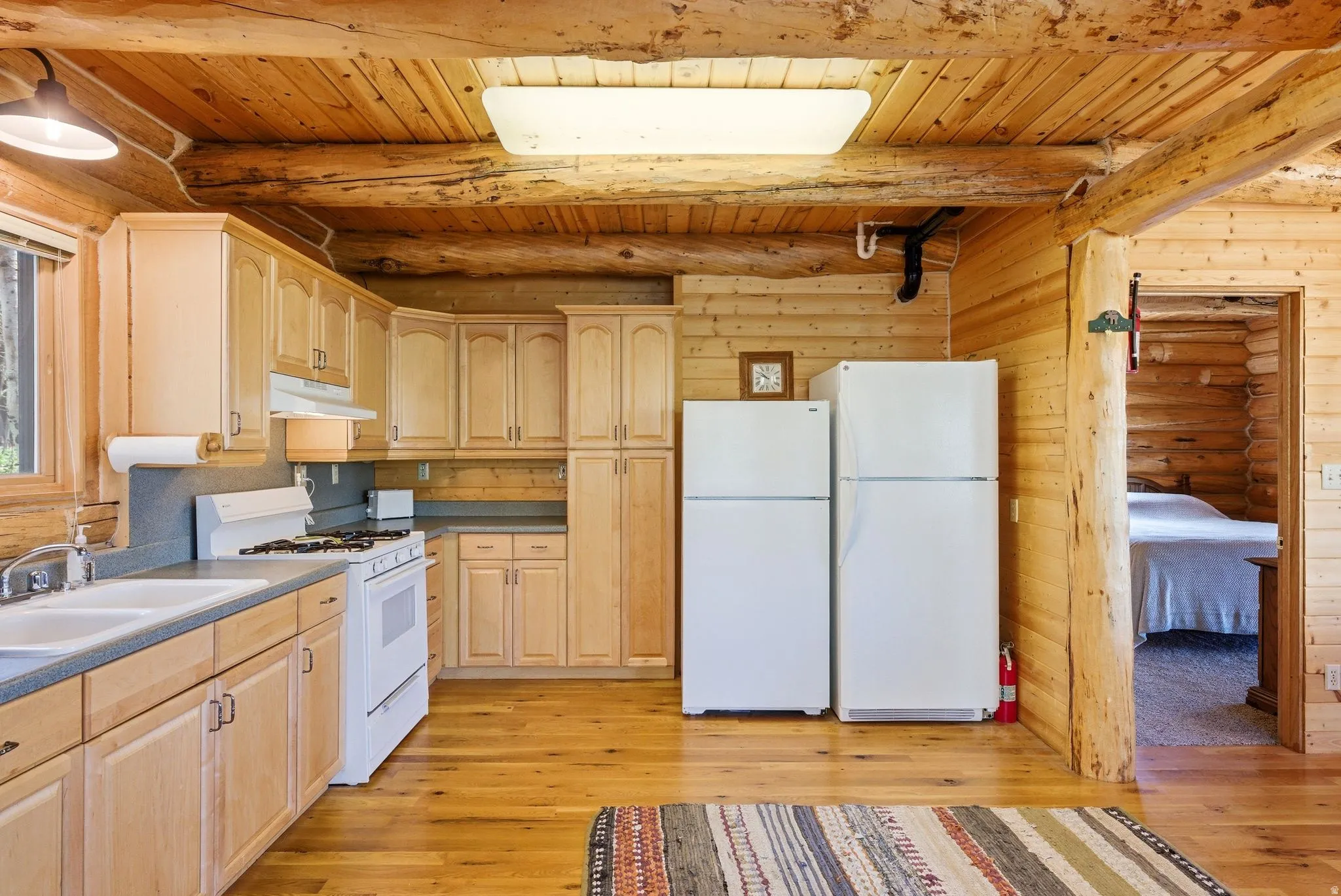 Kitchen featuring light wood cabinetry, a double basin sink, a gas range, and wood-finish flooring