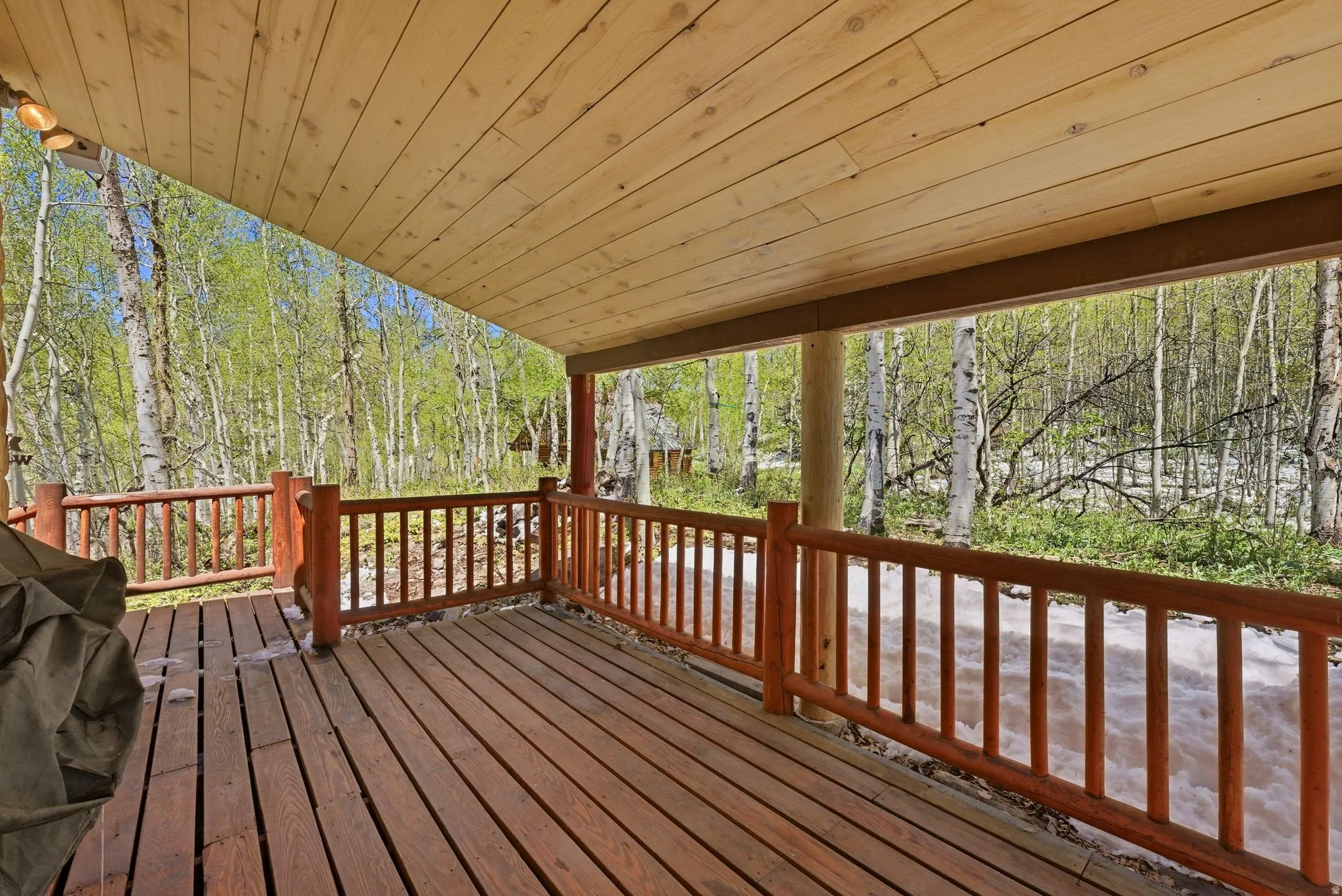 Covered wood deck featuring exposed wood ceiling planks, wood-finish flooring, and a log-style railing
