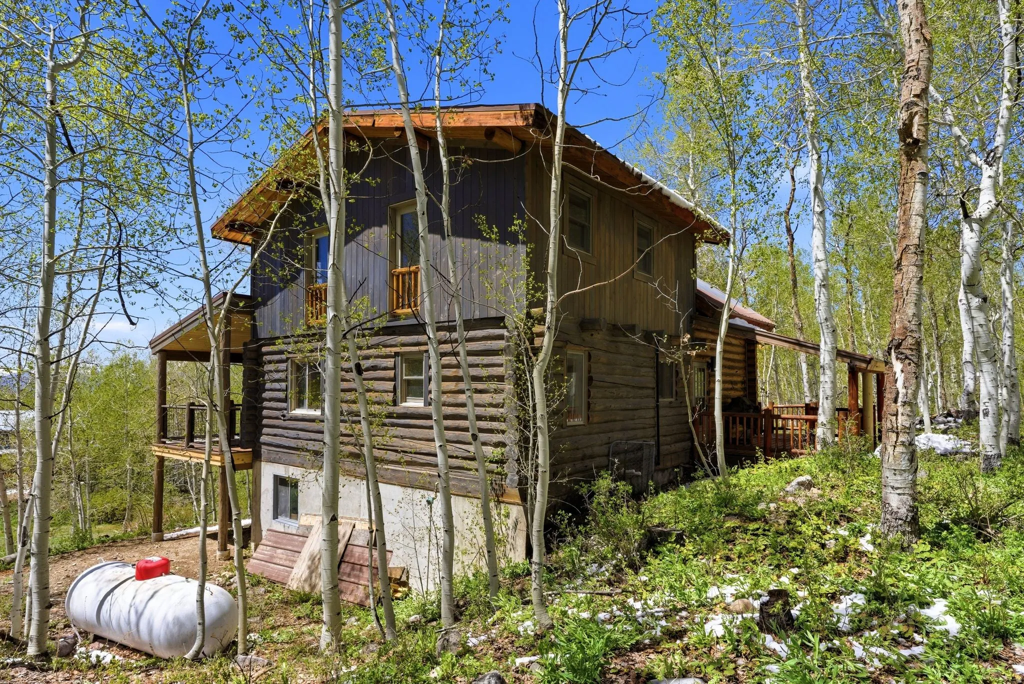 Multi-level log cabin exterior featuring a covered porch, an upper-level balcony, and a sloped metal roof