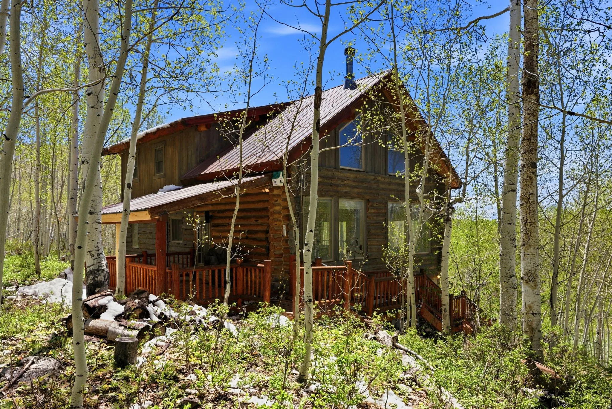 Log cabin exterior featuring a covered porch with wood railing, a metal roof, and exposed wood siding