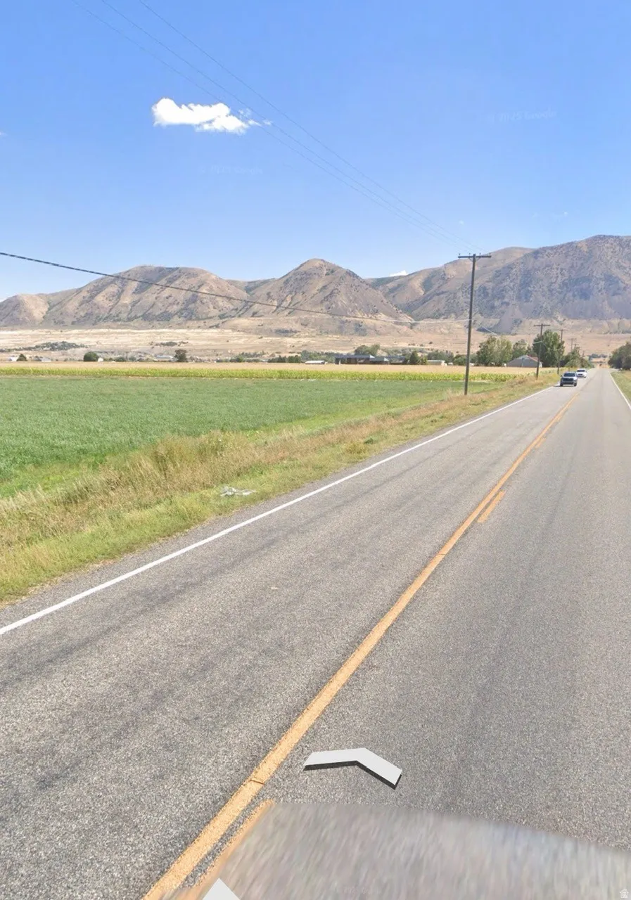Paved road frontage bordering agricultural fields with distant mountains under a clear sky