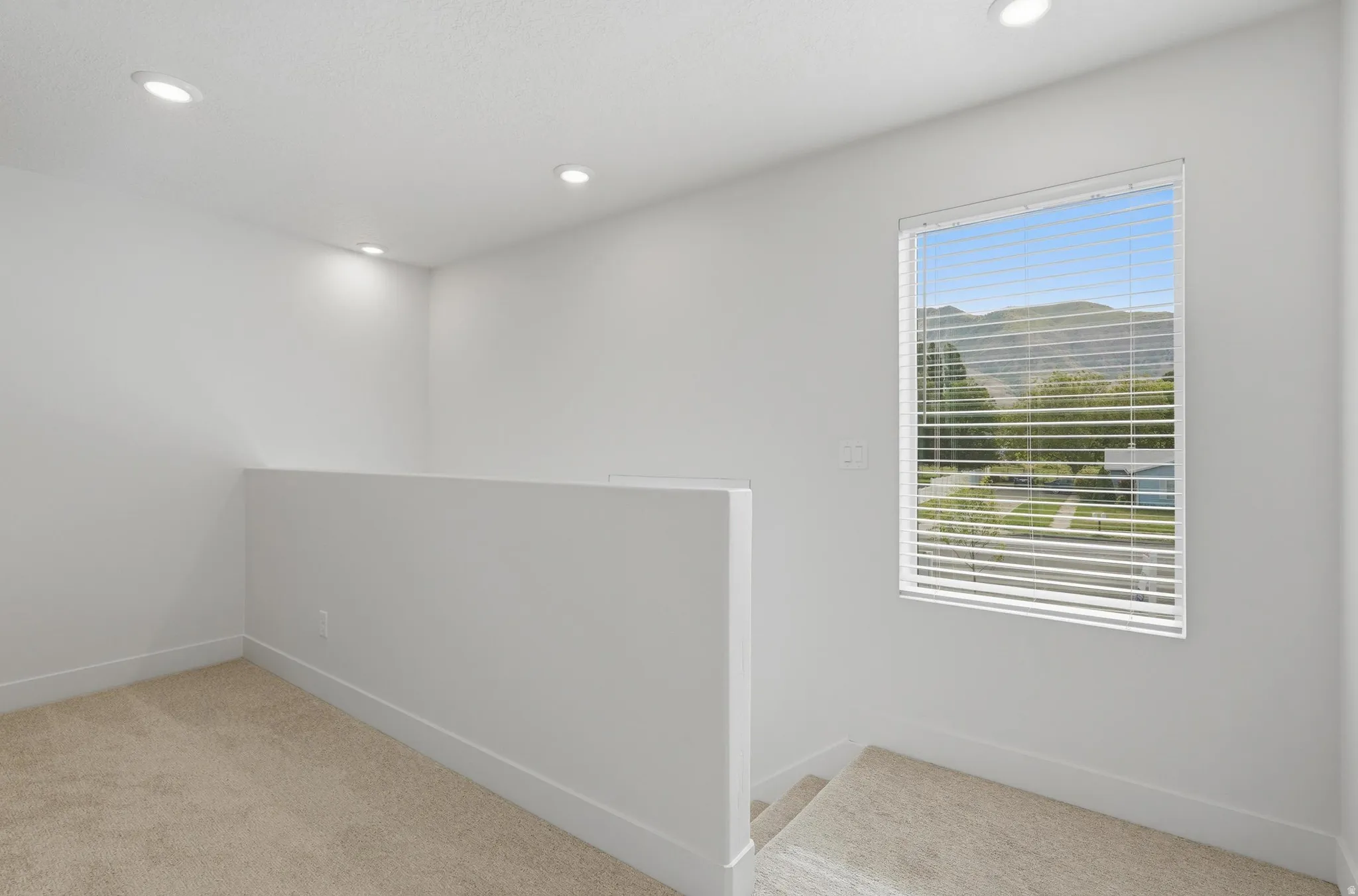 Loft area featuring recessed lighting, a carpeted floor, and a window with blinds overlooking distant mountains and trees