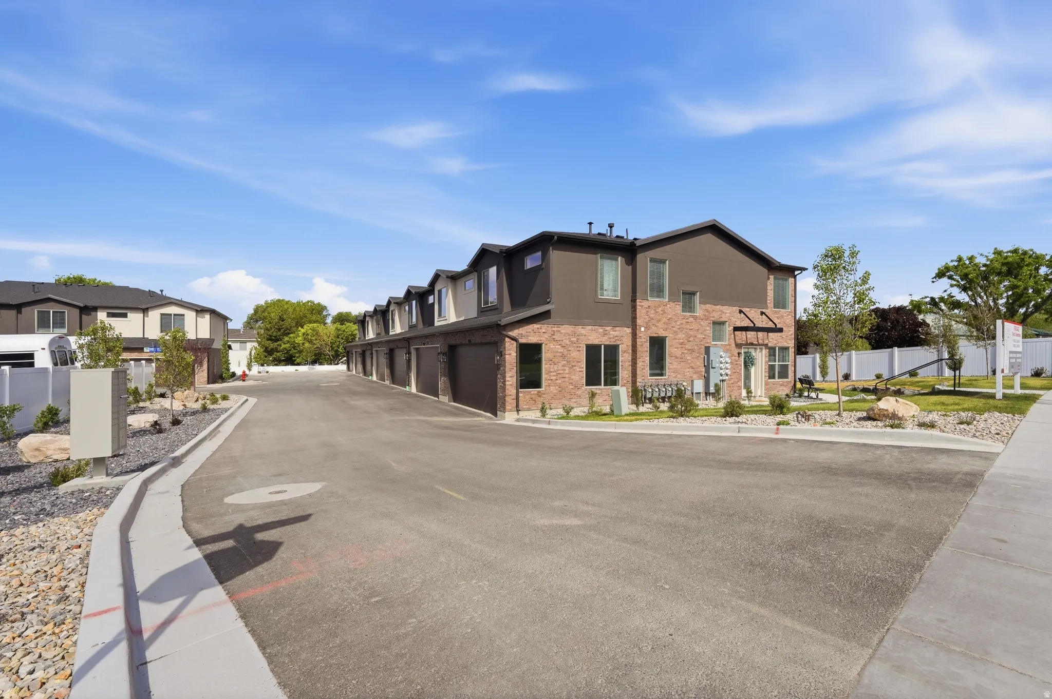 Modern townhome complex featuring brick and dark siding exteriors, individual garages, and landscaped grounds with mature trees
