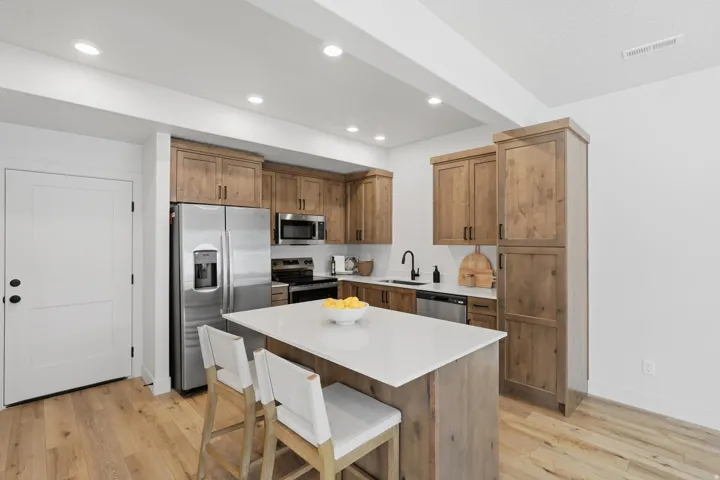 Contemporary kitchen featuring light wood-finish cabinetry and flooring, a white island countertop, stainless steel appliances, and recessed lighting