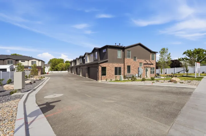 Modern townhome complex featuring brick and dark siding exteriors, individual garages, and landscaped grounds with mature trees