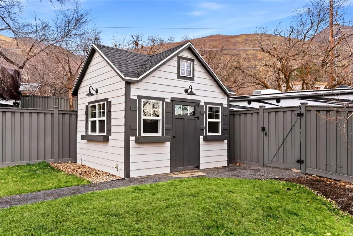 Detached storage shed with gable roof, white siding, dark trim, and decorative exterior lighting