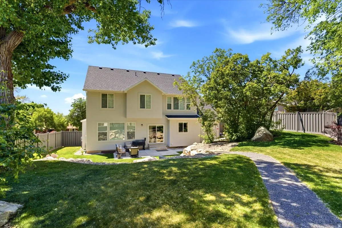 Expansive backyard featuring a manicured lawn, mature trees, and a stone-paved patio