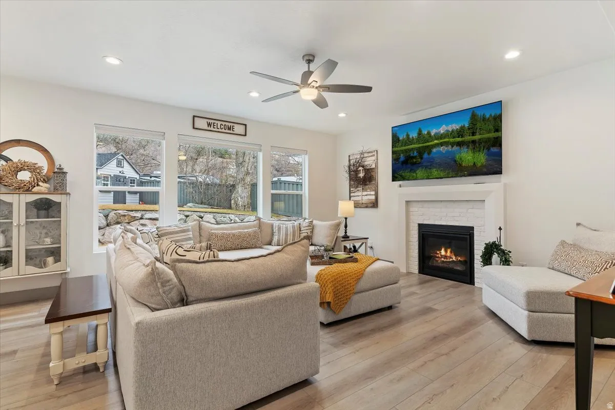 Living area featuring wide plank wood-finish flooring, a white brick fireplace with a substantial mantel, and recessed lighting