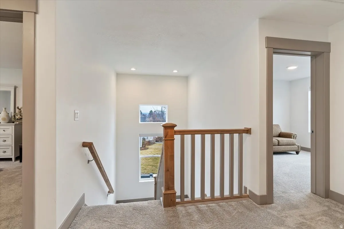 Carpeted hallway featuring a wood and painted baluster railing, recessed lighting, and a square window