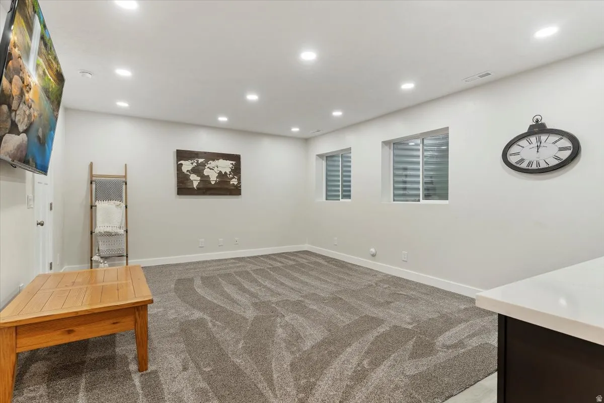 Spacious room with recessed lighting, light gray walls, two windows with horizontal blinds, and patterned carpeting